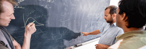 three physicists work on equations on a chalkboard