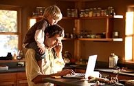 Man working at home with child on his shoulders.