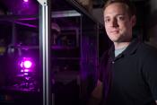 Photo - Tim Miller standing in dark room beside glowing purple point of light